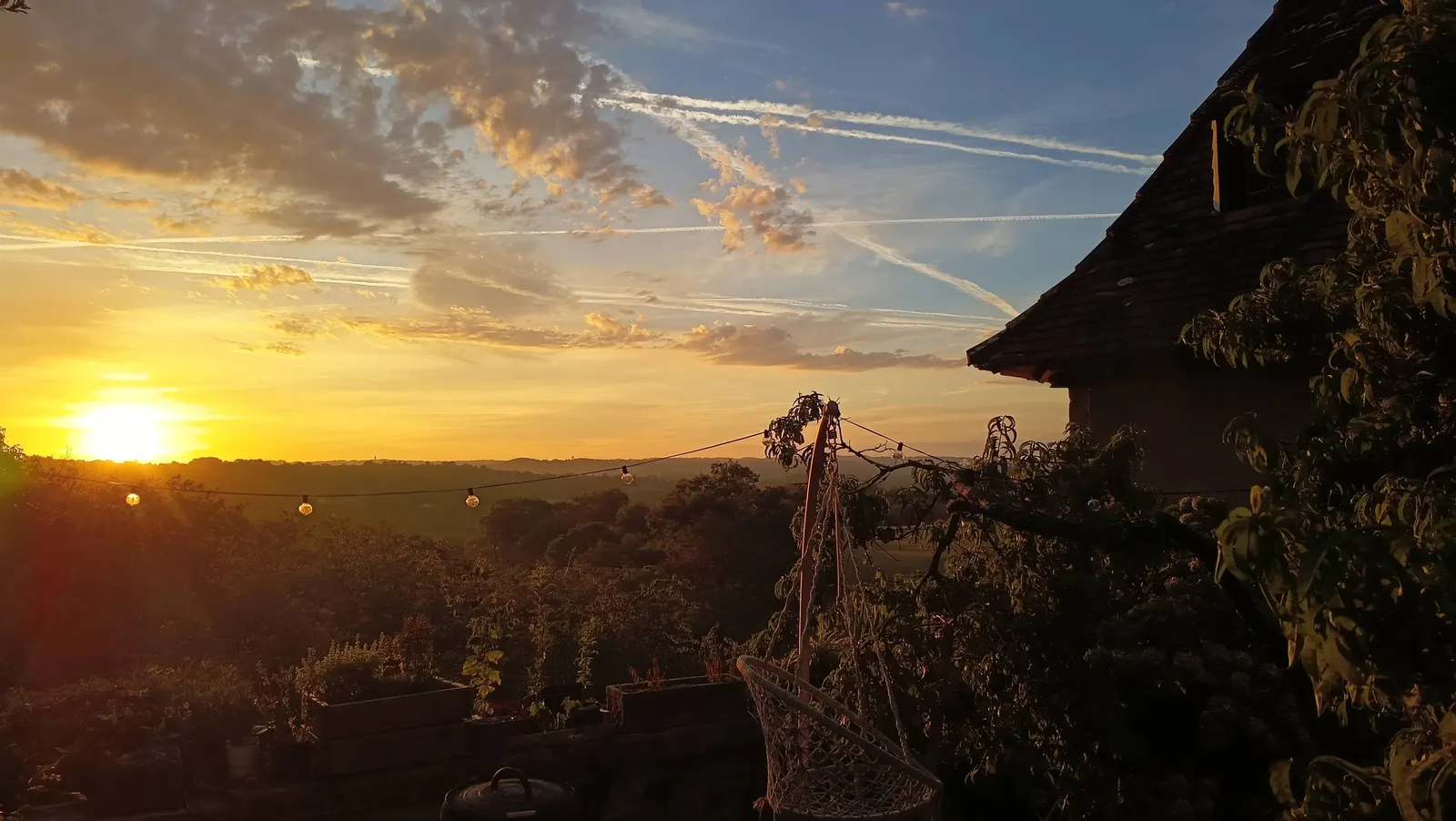Coucher de soleil doré sur la terrasse, guirlande lumineuse se découpant devant un ciel strié de traînées de nuages