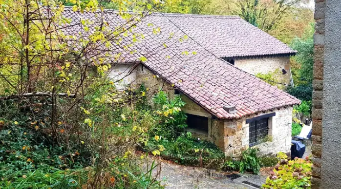 Dépendance en pierres de taille de La Fontaine du Mas vue depuis le jardin en automne, toiture en tuiles rondes, végétation aux couleurs jaunes et orangées, chemin dallé menant à l'entrée