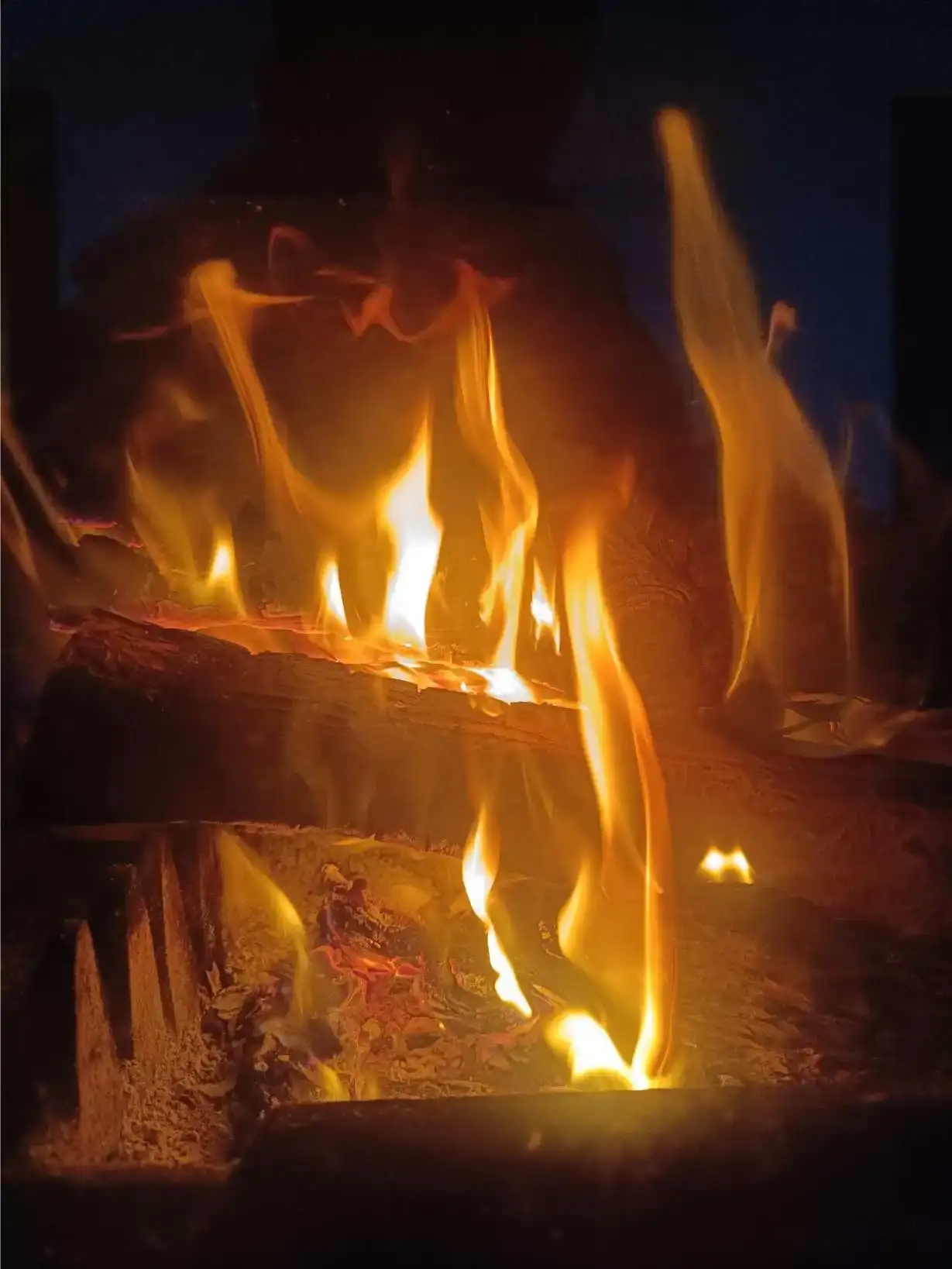 Flammes vives et dansantes photographiées en gros plan dans le foyer de la cheminée de La Fontaine du Mas, bûches incandescentes en braise, image chaleureuse et hypnotique