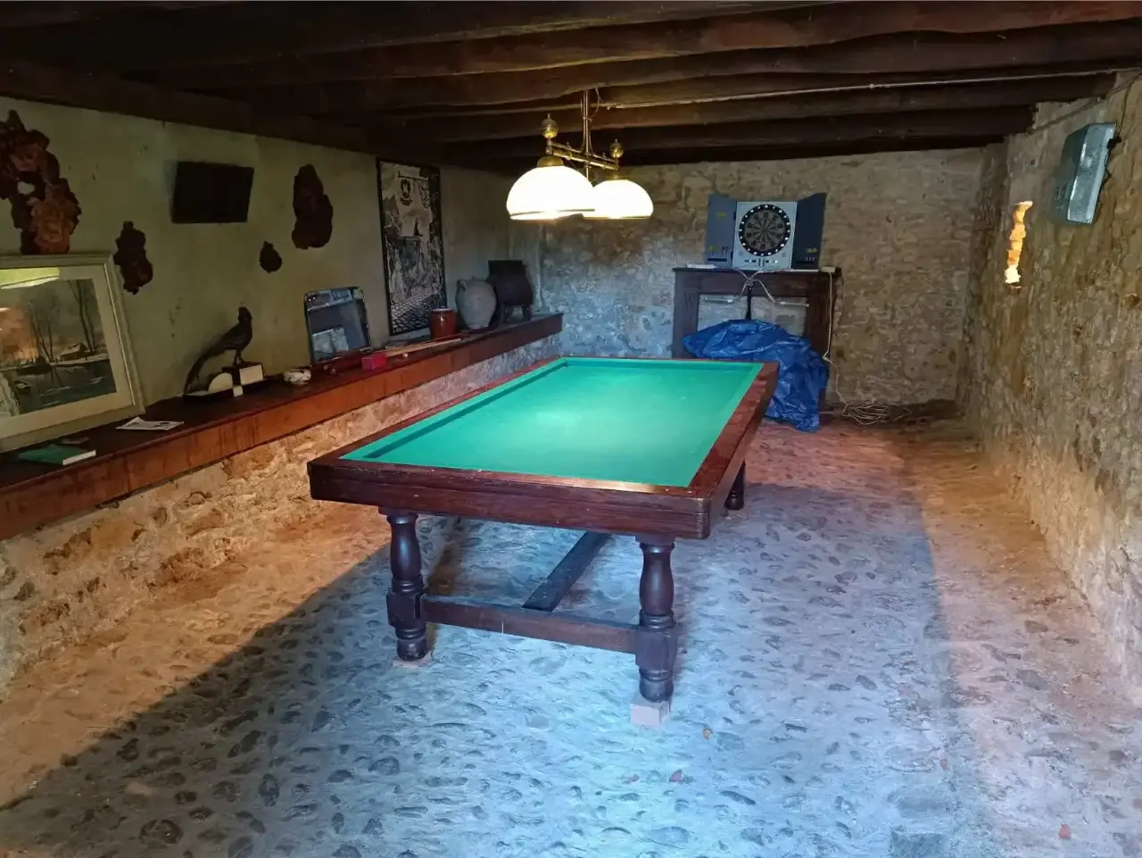 Salle de jeux de La Fontaine du Mas, autre angle : billard français tapis vert sous un luminaire à double abat-jour, murs en pierres, décorations et tableaux anciens