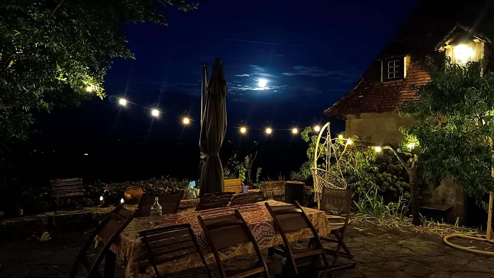 Table dressée pour un dîner en extérieur sous la pleine lune, éclairée par une guirlande guinguette et des lanternes